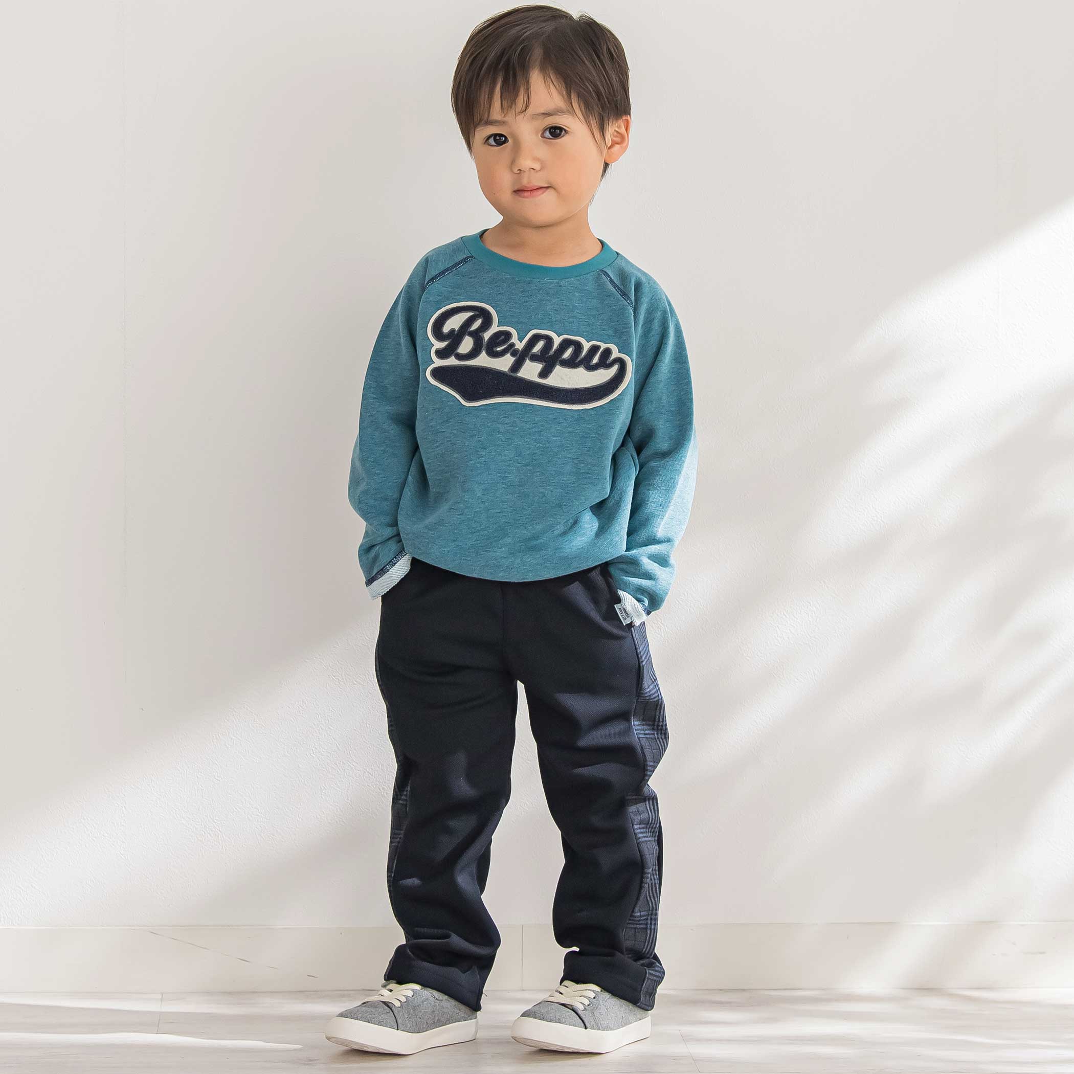 BeBe Petits Pois Vert サガラワッペントレーナーとサイドチェックパンツを着てジャンプする男の子の全身コーディネート画像