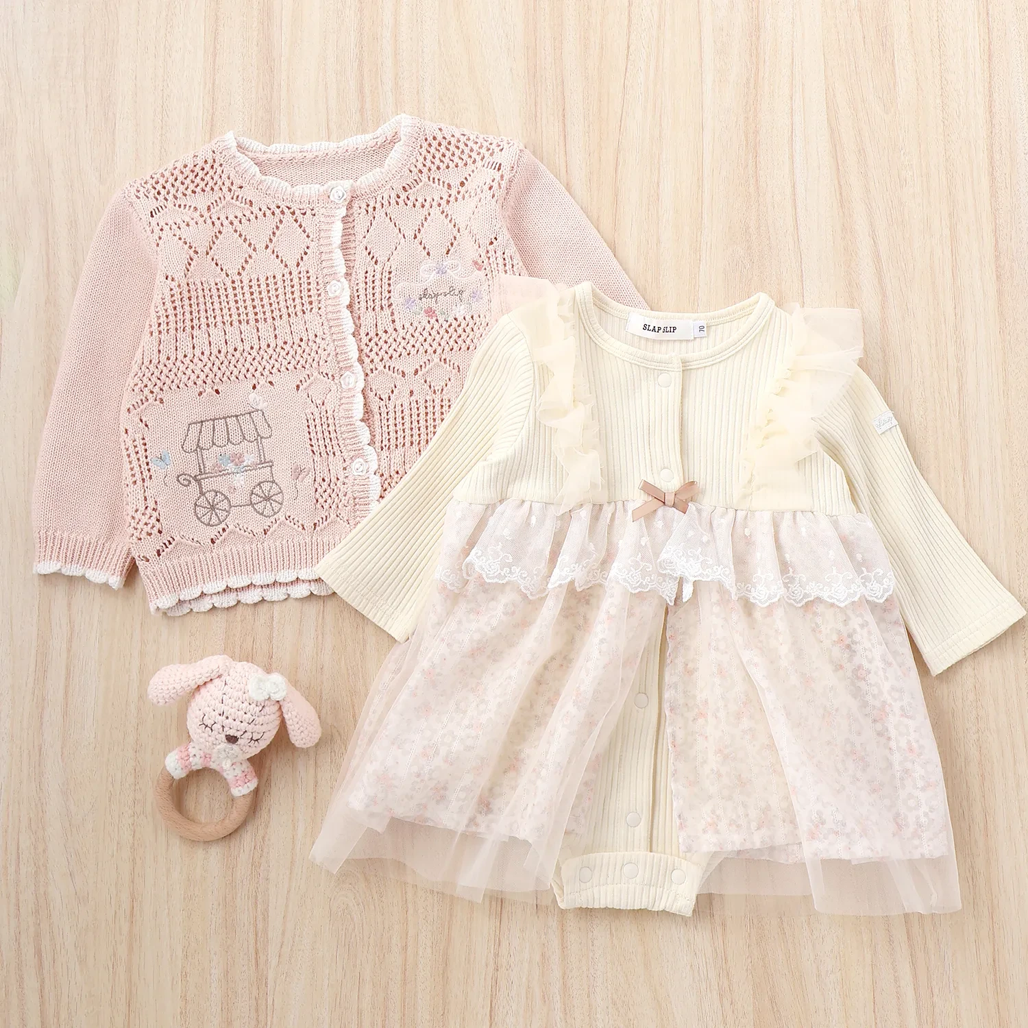 チュールとフリルたっぷりのロンパースとレース編みのニットカーディガンでにうさぎさんのラトルも一緒に
